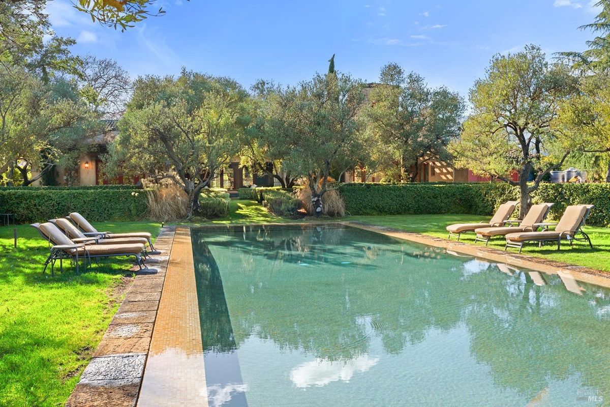 A swimming pool set within a manicured lawn, surrounded by trees. Lounge chairs are positioned along the poolside.