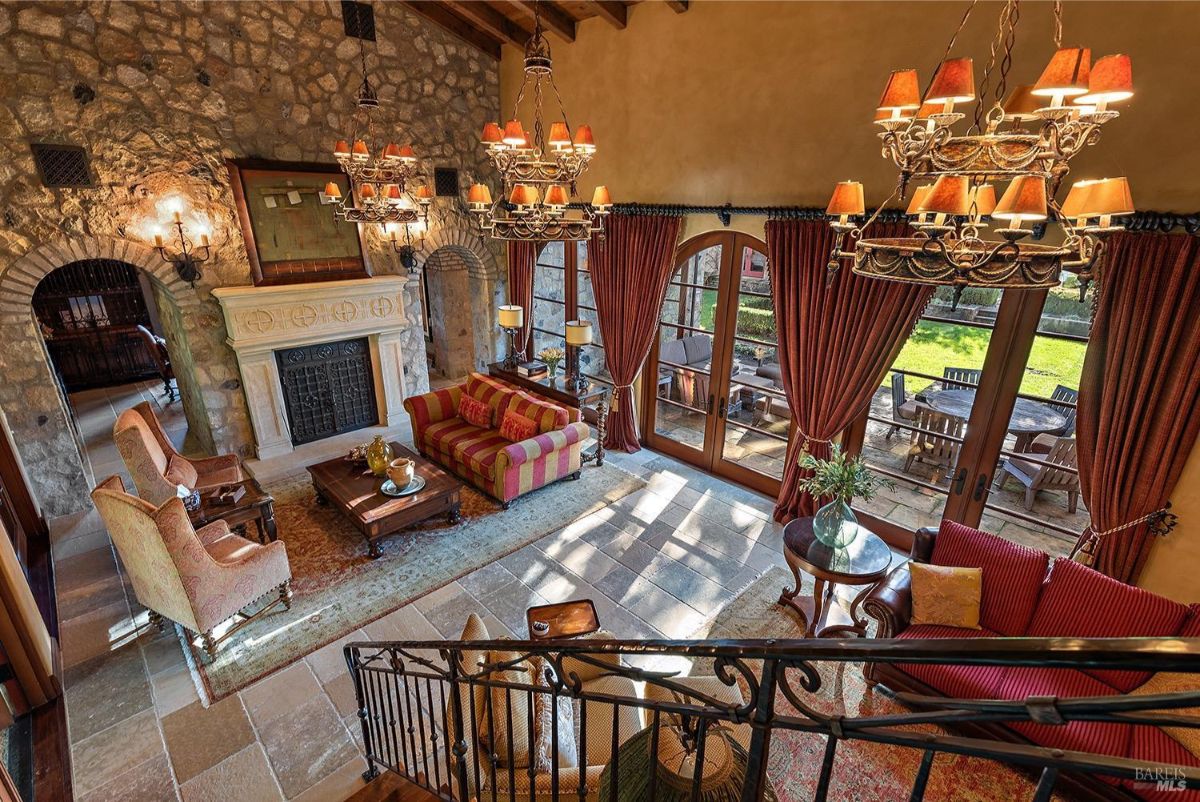  A top-down view of the same living room highlighting the seating area, stone fireplace, and outdoor patio visible through large glass doors.