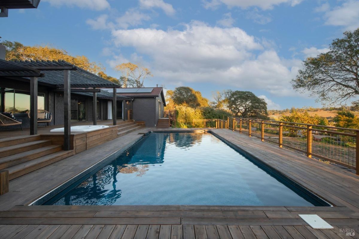 Outdoor pool with a wooden deck and attached house featuring a pergola.