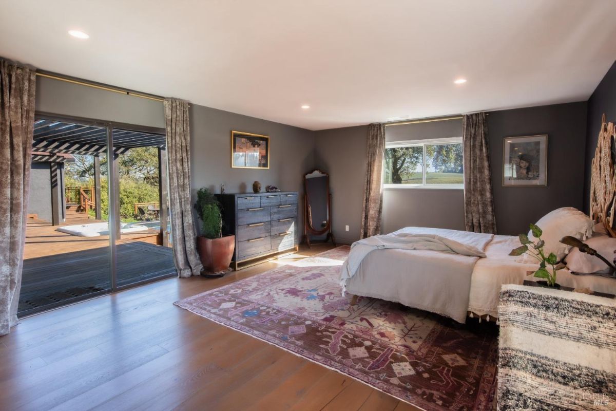 Spacious bedroom with a sliding door opening to a deck, featuring a large rug, dresser, and simple decor.