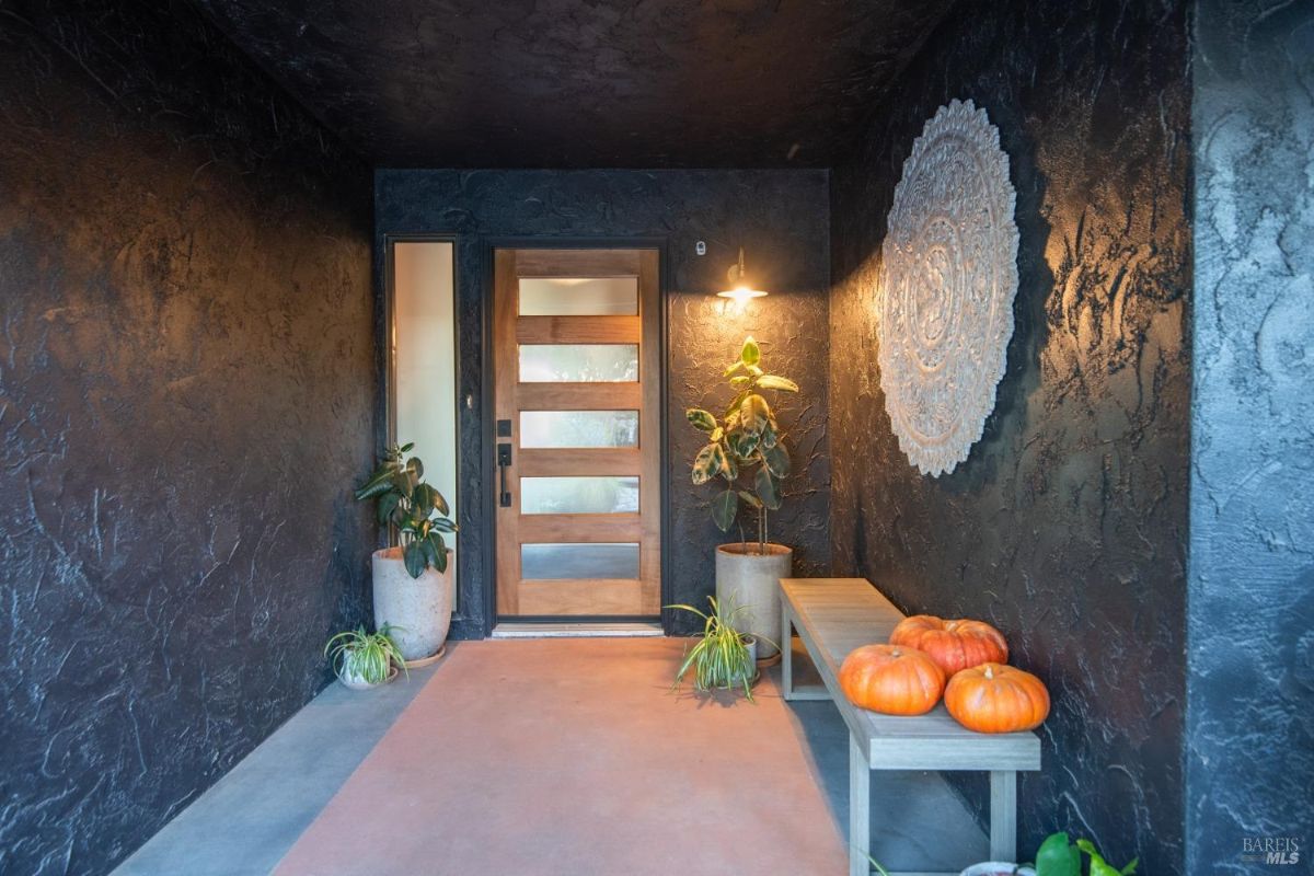 Covered front porch with textured walls, a wooden door, and decorative pumpkins.