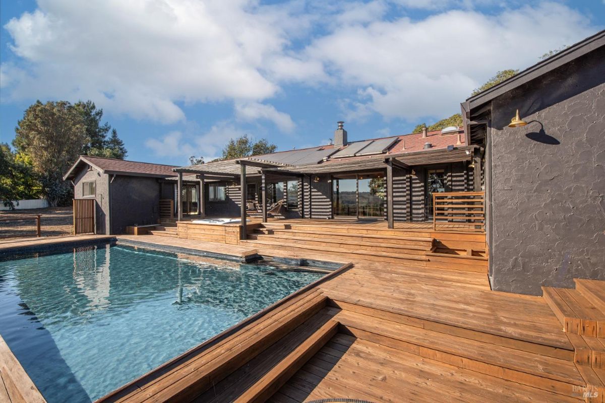 Outdoor pool with a wooden deck and pergola extending from the house.