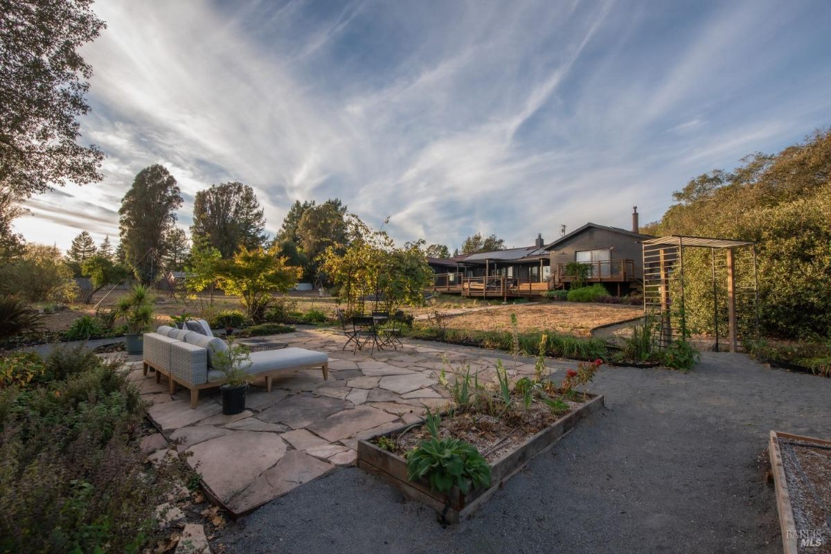 Wide view of the patio and garden space with the house in the background and open skies above.