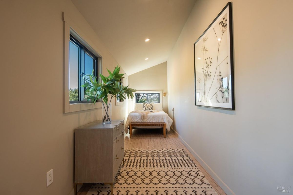 Long narrow hallway leading to a small bedroom with a bed and natural light from windows on both sides.