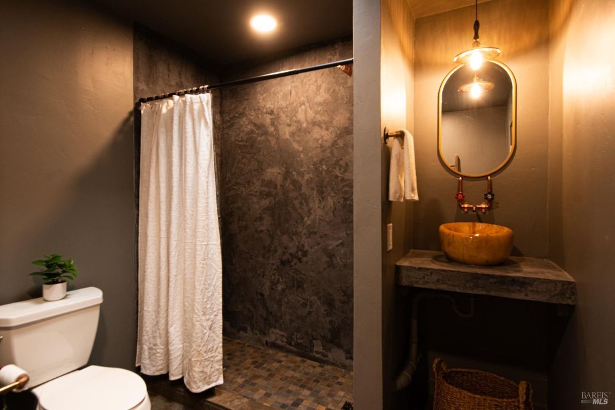 Bathroom featuring a textured shower, white curtain, modern sink, and gold-accented mirror.