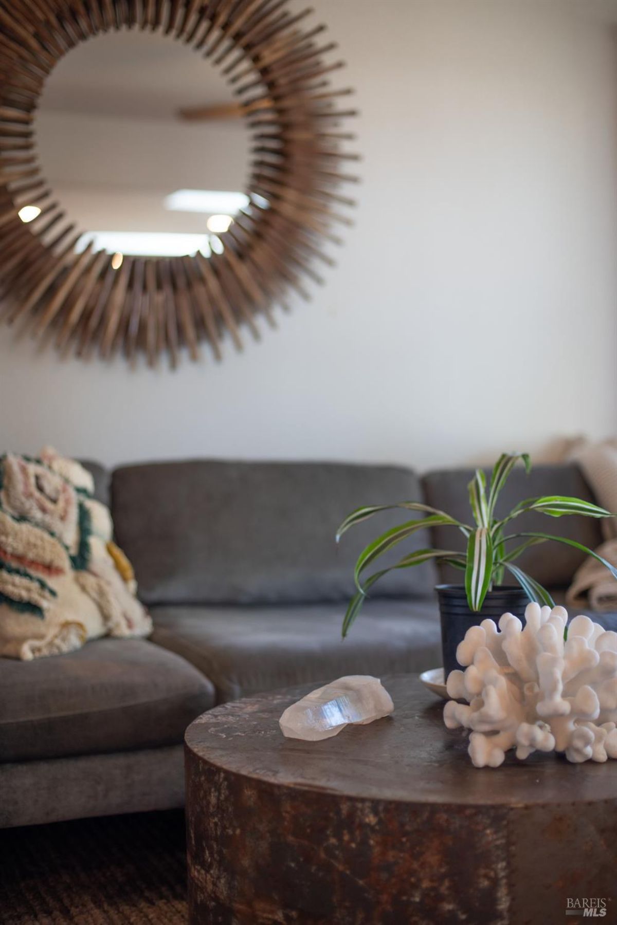 Close-up of a round decorative mirror above a gray sofa with a wooden coffee table and decorative items.