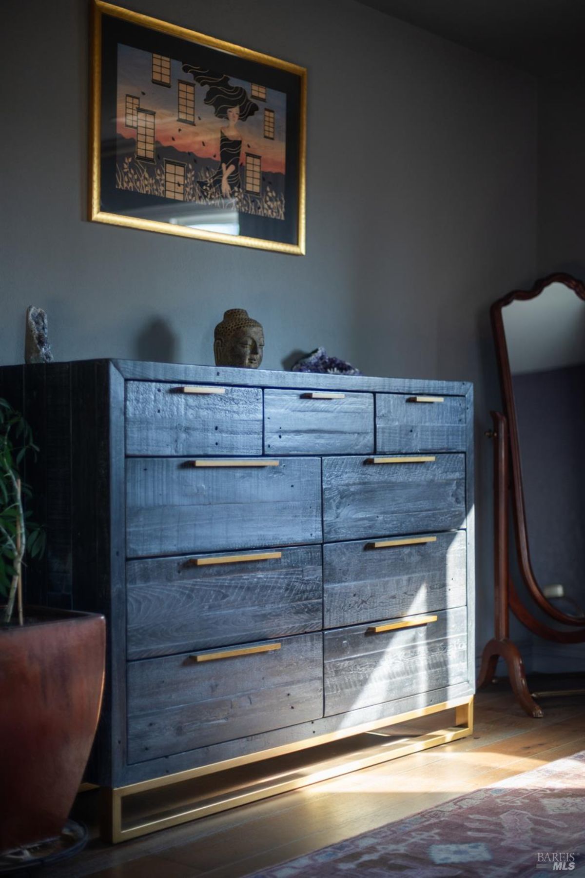 Wooden dresser with golden handles, adorned with a framed artwork and small decorative items on top.