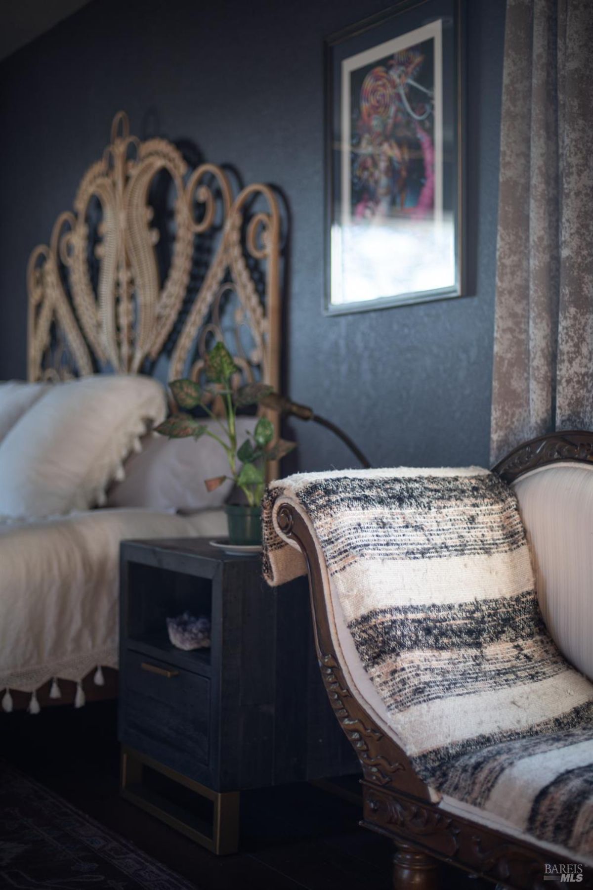 Close-up of a decorative chair with a striped blanket next to a bedside table and a detailed headboard.