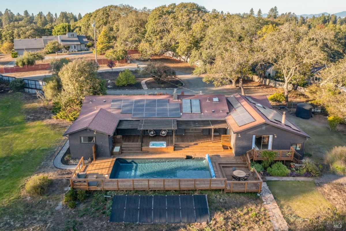 Backyard pool area with a wooden deck, solar panels on the roof, and a spa.