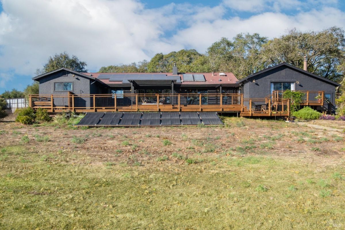 Back view of a house with solar panels, wooden decking, and landscaped surroundings.