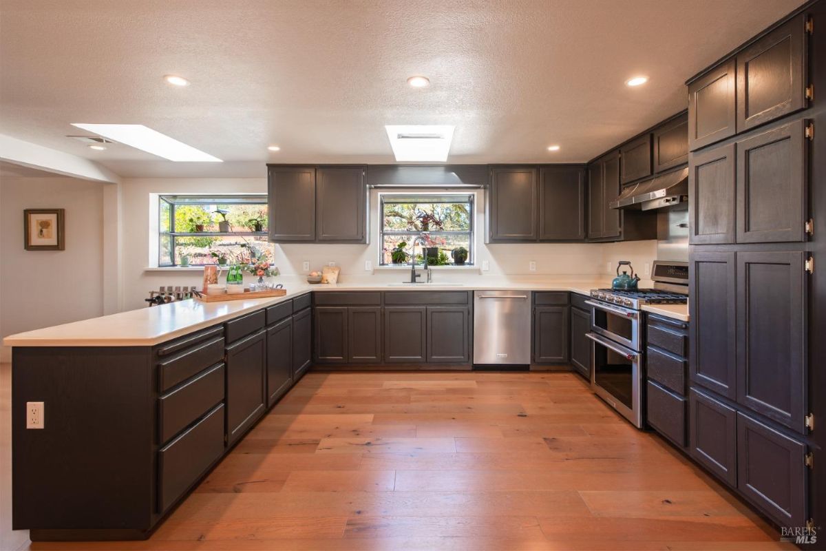 Spacious kitchen with dark cabinets, light countertops, and wood flooring, featuring ample natural light.