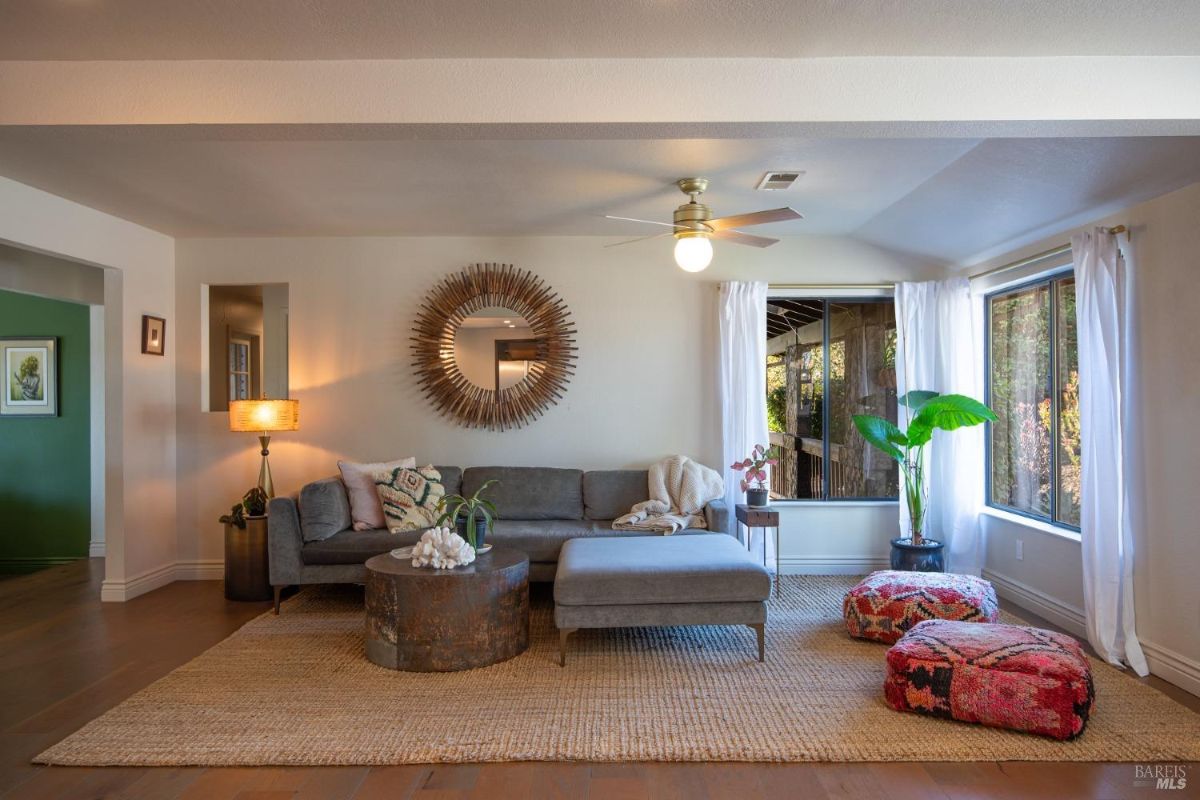 Cozy living room with a gray sectional sofa, natural light, and colorful poufs on the floor.