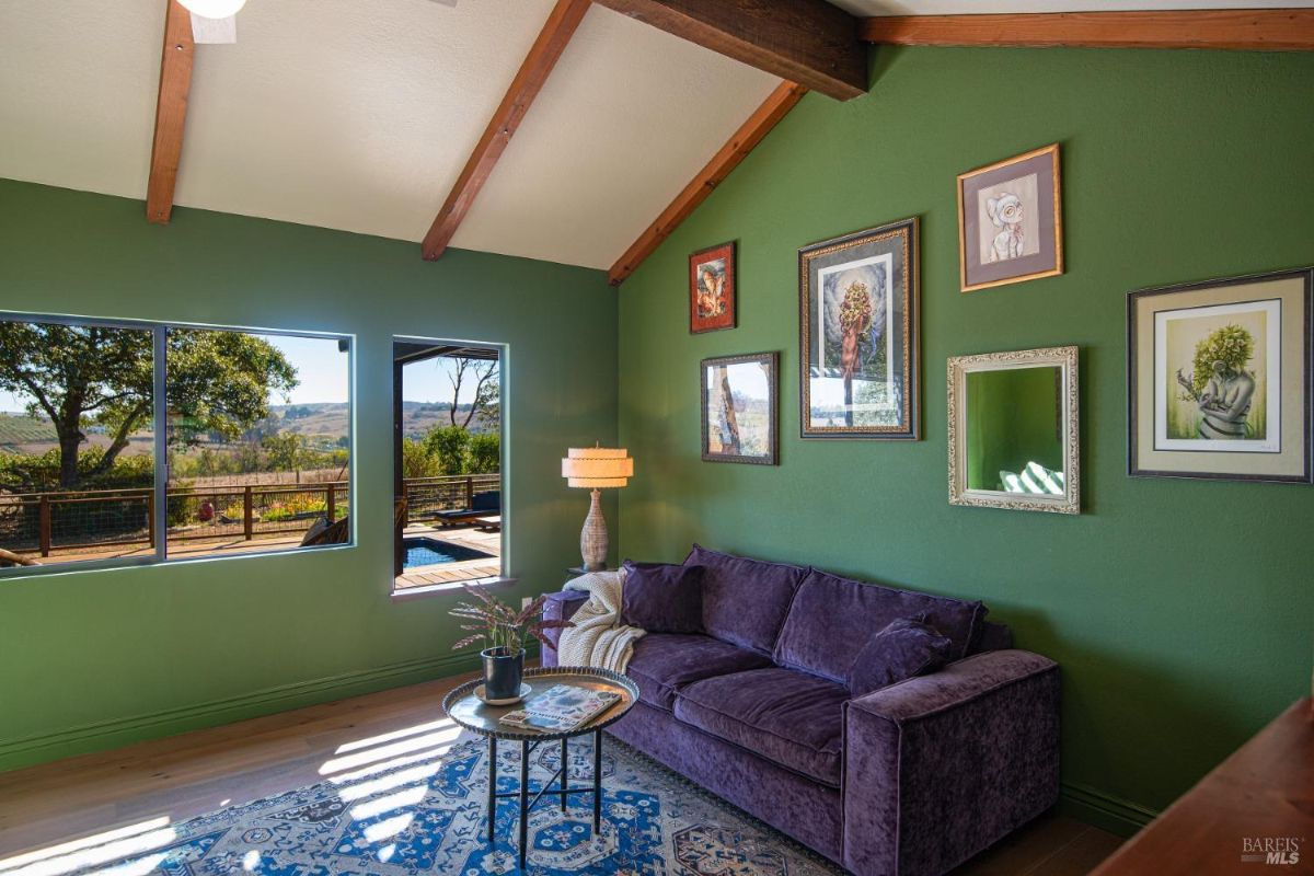 Small sitting room with a green accent wall, a purple couch, and framed artwork.