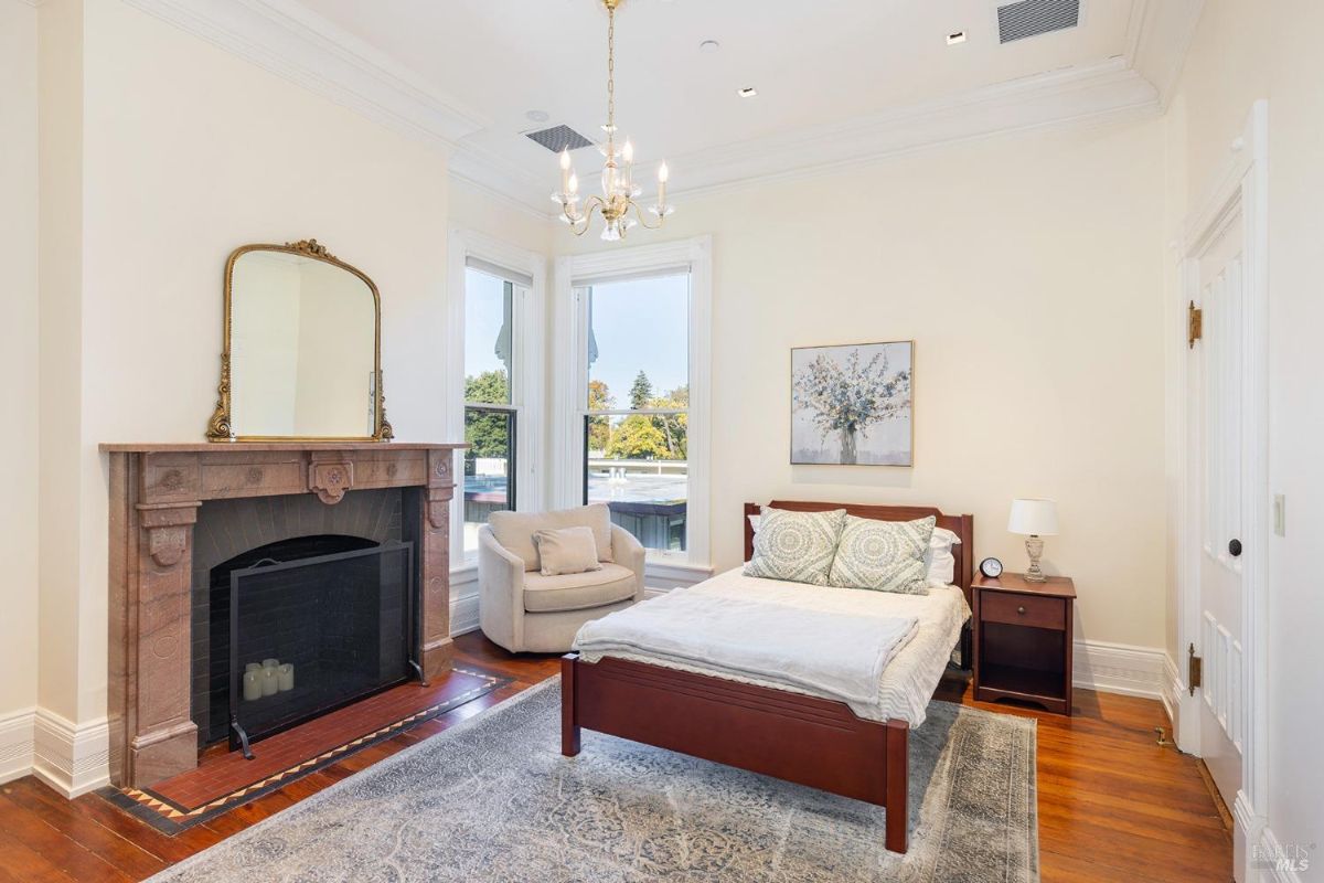  A minimalistic yet charming bedroom with a fireplace, a comfortable bed, and a cozy armchair. The room's large windows and tasteful artwork provide a tranquil ambiance.