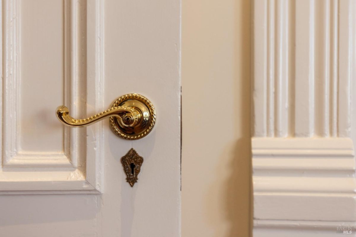 A detailed image of a golden door handle on a white paneled door, showcasing intricate craftsmanship and vintage charm.