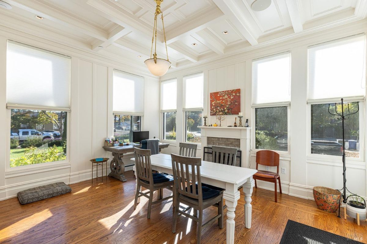 A multifunctional room with an elongated table and more natural light. The fireplace is a central feature, surrounded by tasteful decorations, creating a welcoming atmosphere.