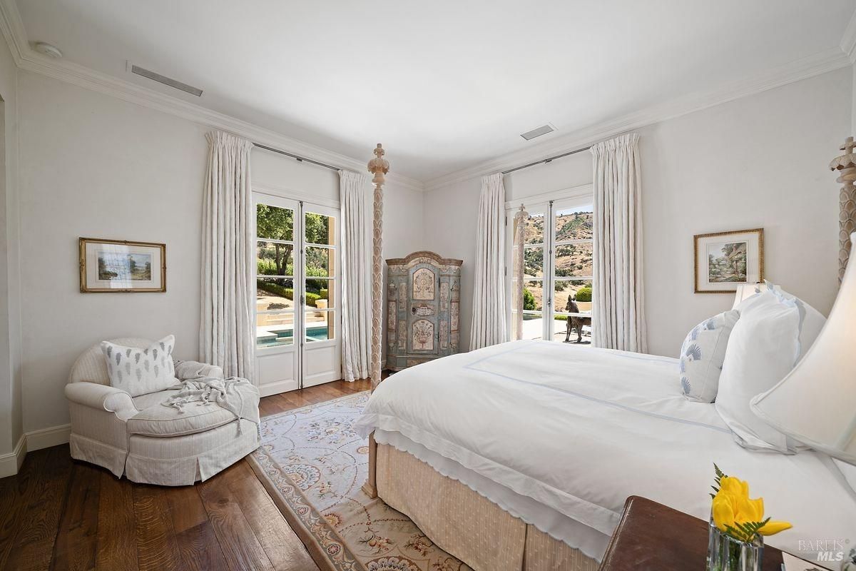 Bedroom with a large bed and French doors open to reveal a view of landscape 