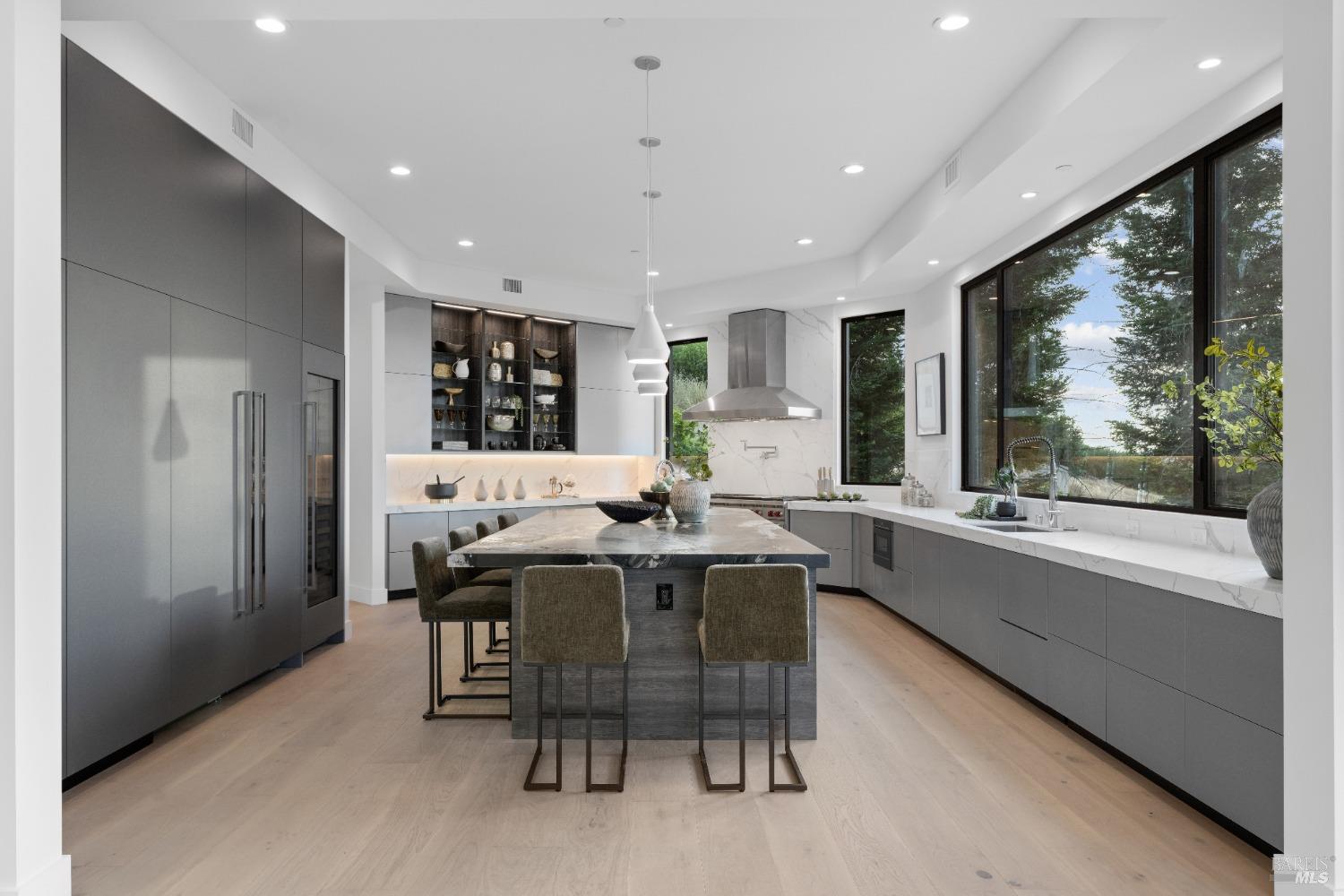 Modern kitchen features a large marble island, sleek cabinetry, and expansive windows.