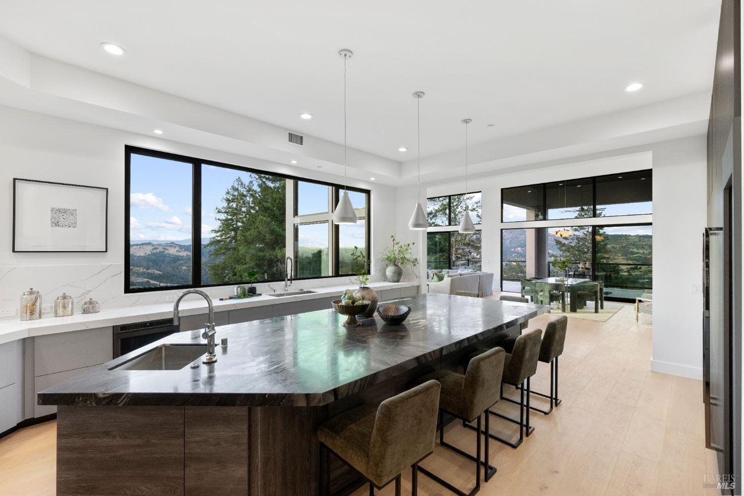 Kitchen island with dark marble countertop and bar stools facing large windows with hillside views.