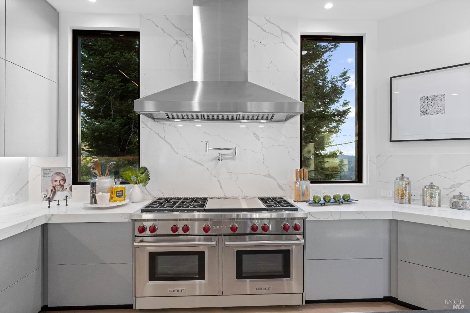 Double oven and range with marble backsplash flanked by windows with outdoor views.