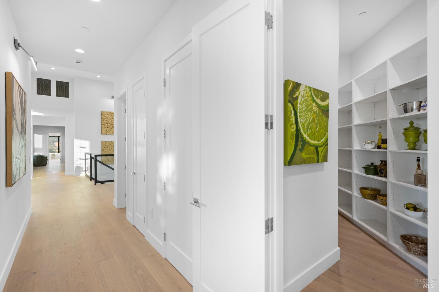 Hallway with white walls, light wood flooring, and access to a pantry with open shelving.