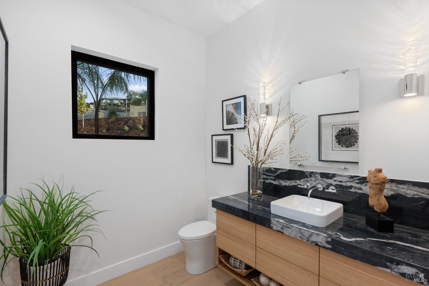 Powder room with black marble countertop, wood vanity, and decorative wall art.