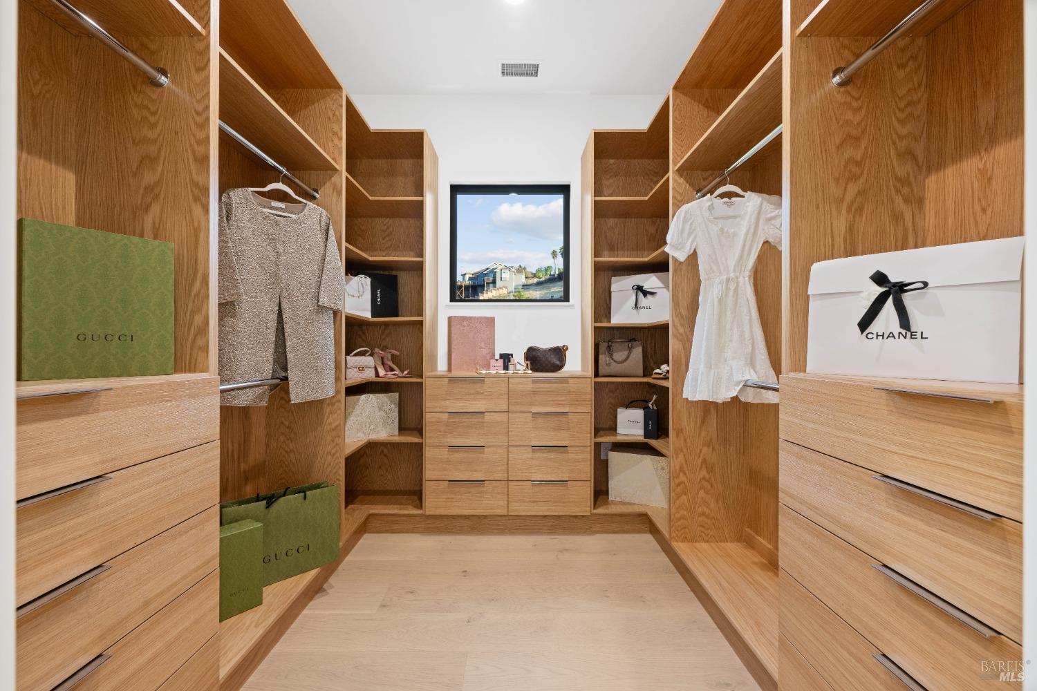 Walk-in closet with custom wooden shelving, drawers, and clothing neatly displayed.