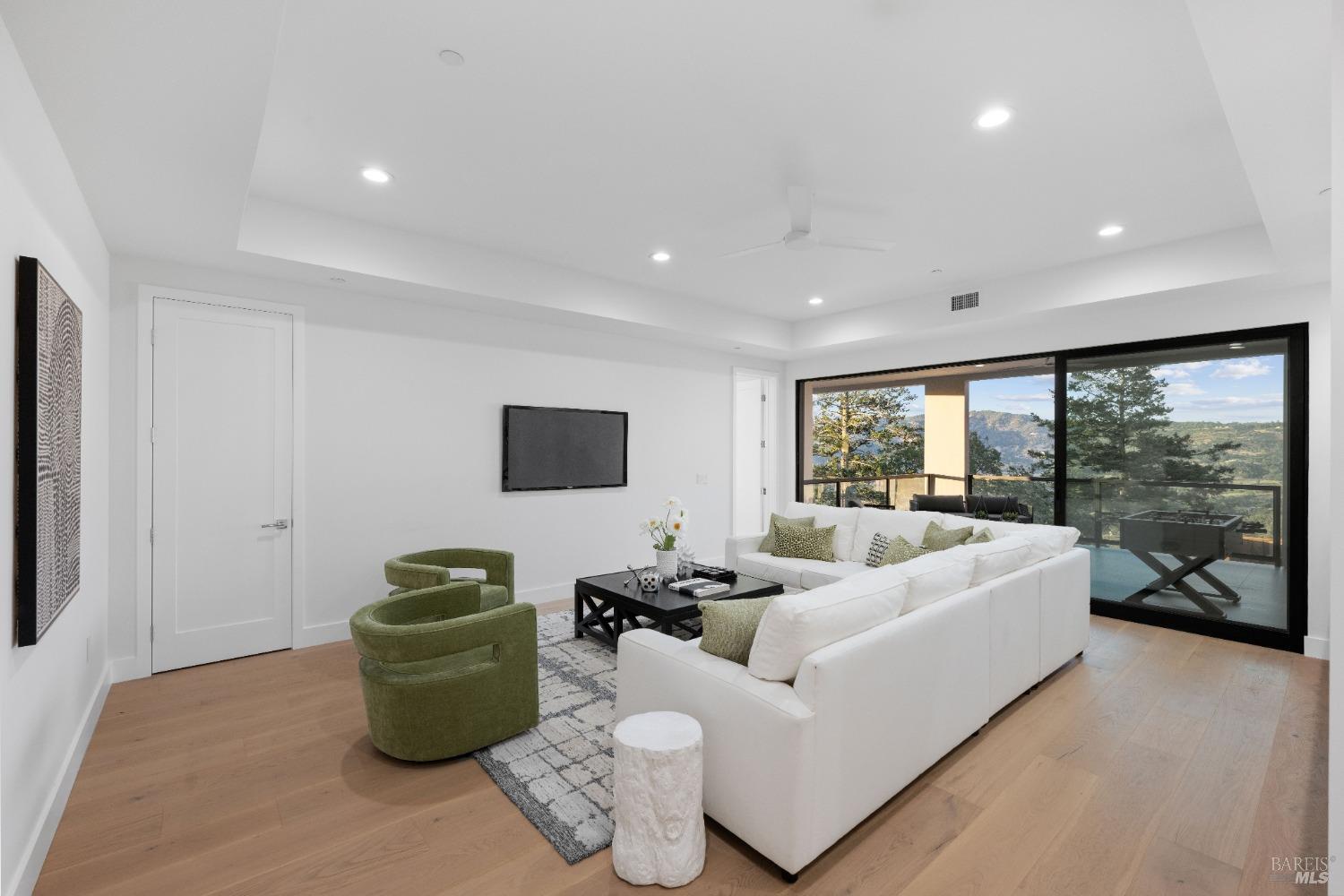 Bright modern living room with white sectional sofa, green armchairs, and a large sliding glass door revealing an outdoor view.