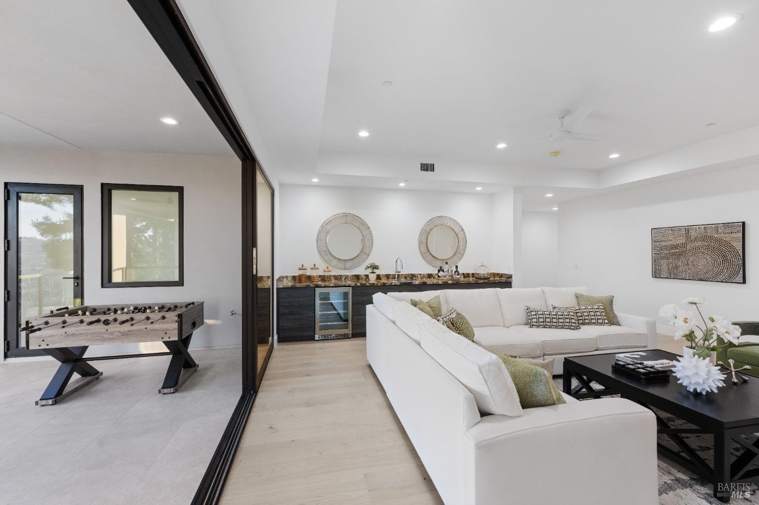 Lounge area with a white sectional sofa, a foosball table, and a bar counter with mirrors.