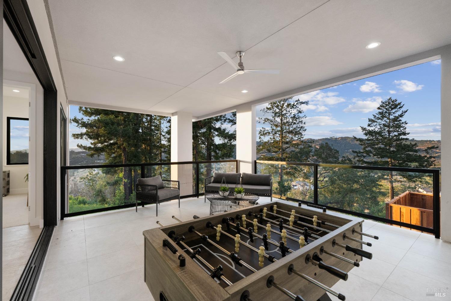 An outdoor patio with a foosball table, seating area, and views of a forested valley.