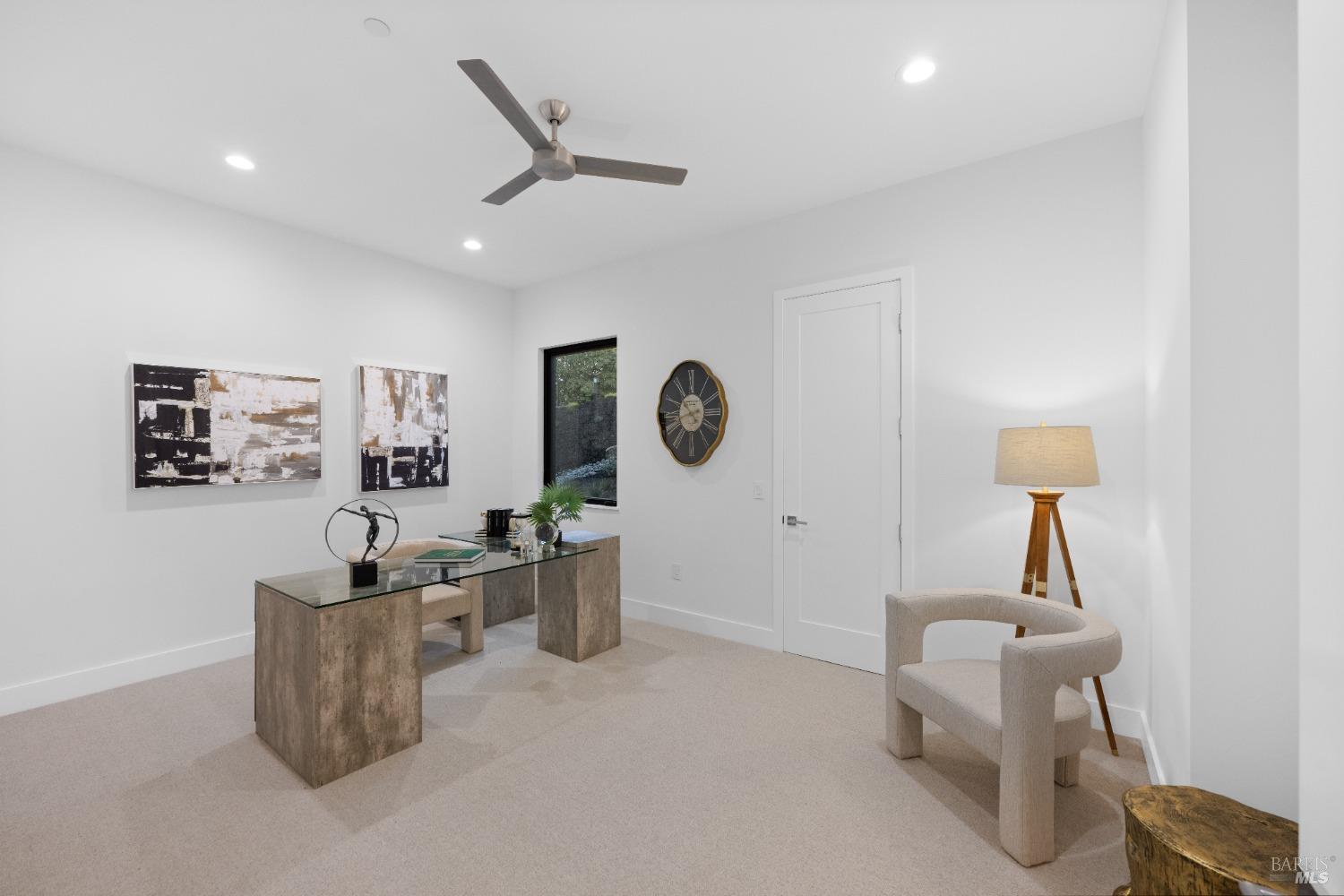 Home office with a glass desk, neutral decor, and a window offering outdoor views.