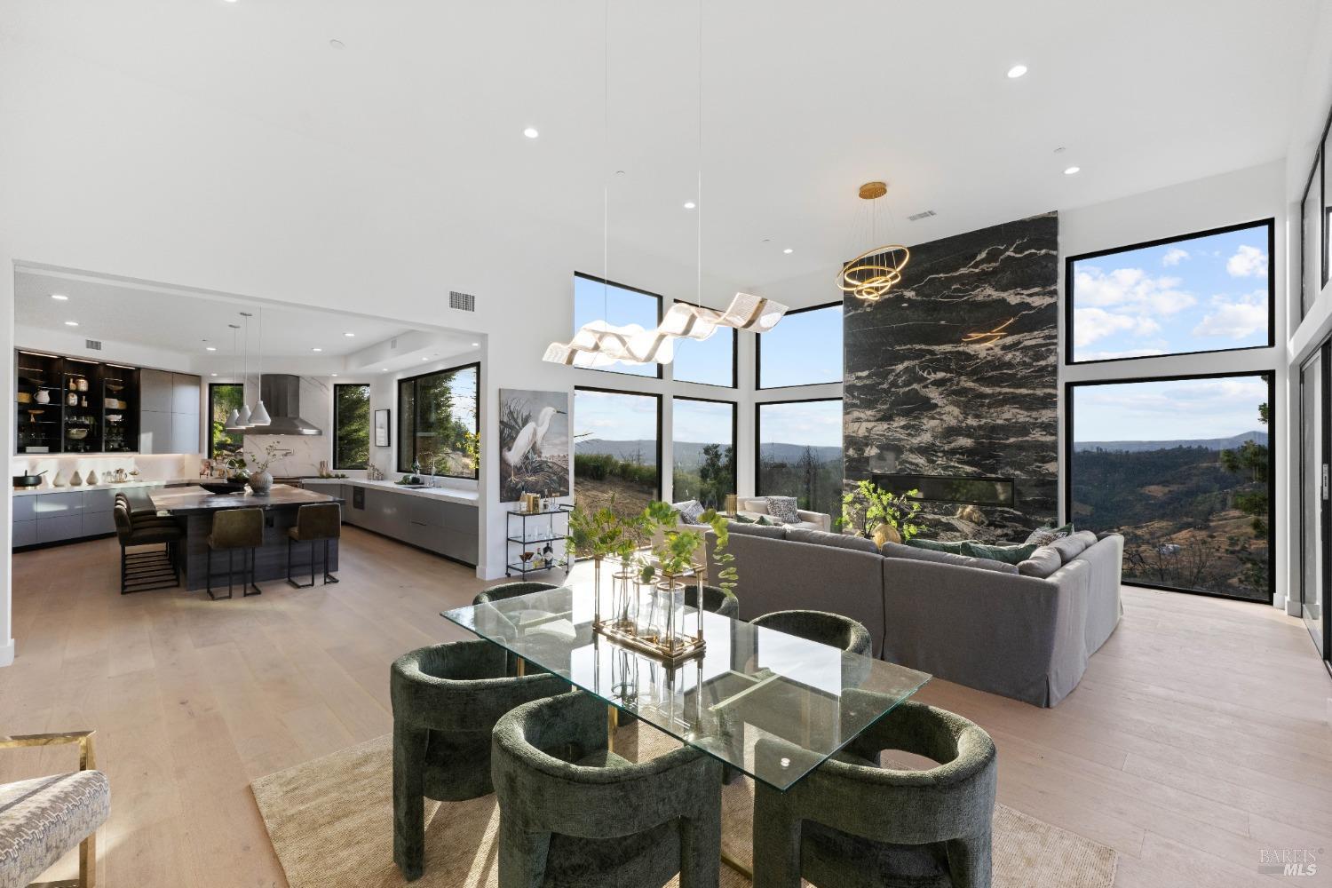 Modern kitchen and dining space connected to the living area, featuring a glass dining table, green chairs, and panoramic windows.