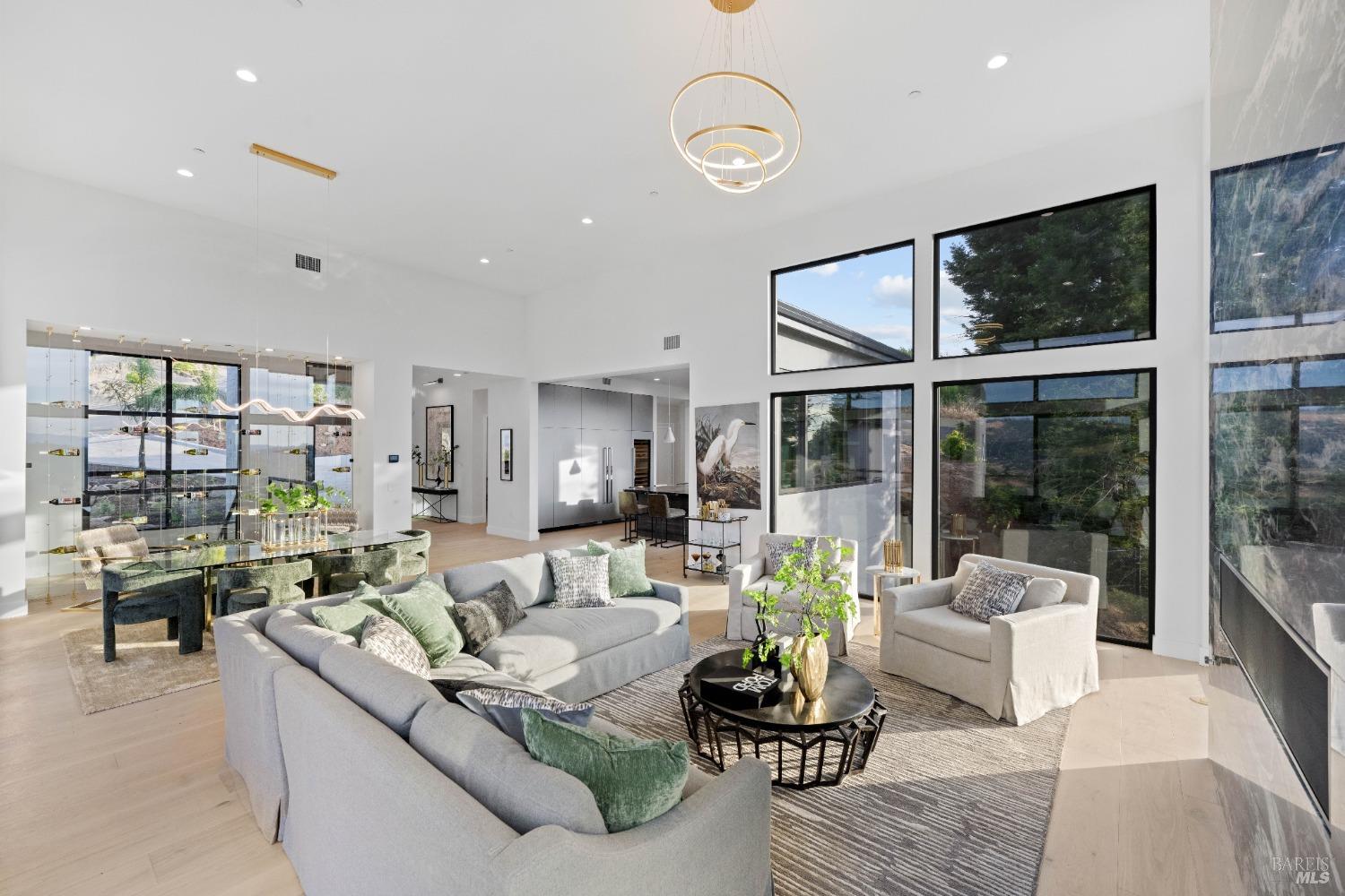 Living room with high ceilings, large windows, and an open floor plan that connects to a dining area.