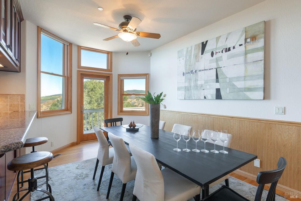 Dining area includes a rectangular table with chairs and large windows offering outdoor views.