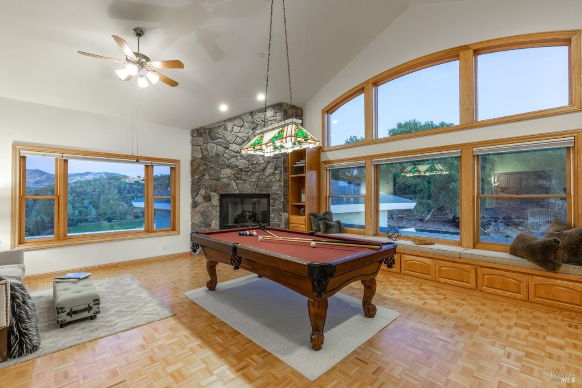 Billiard room with stone fireplace, pool table, and large windows.