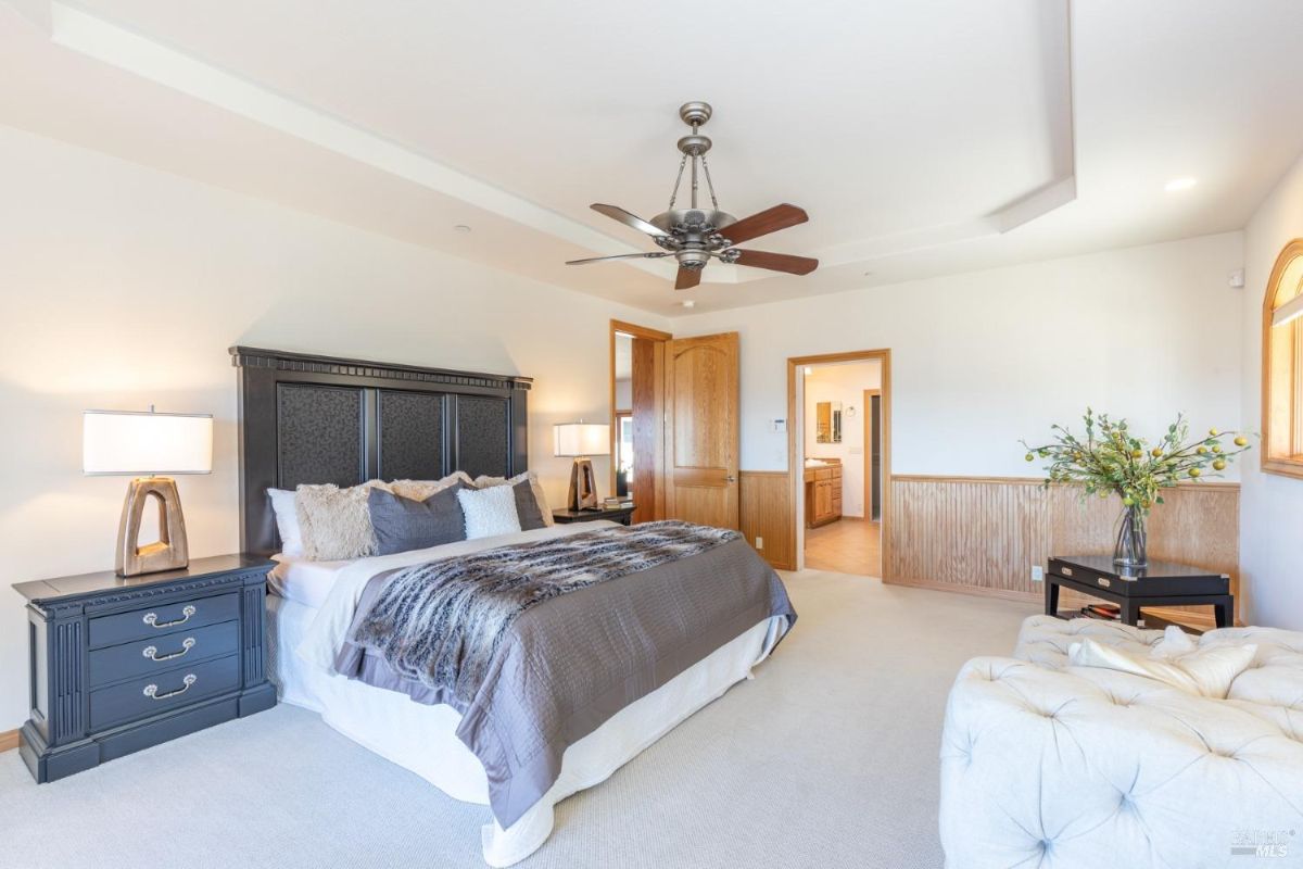 Bedroom with a dark wood bedframe, ceiling fan, and en suite bathroom visible through an open door.