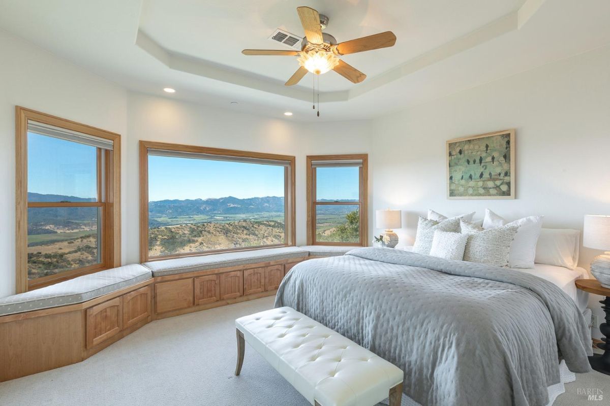 Master bedroom with large bay windows, a bench seat, and views of the surrounding hills.