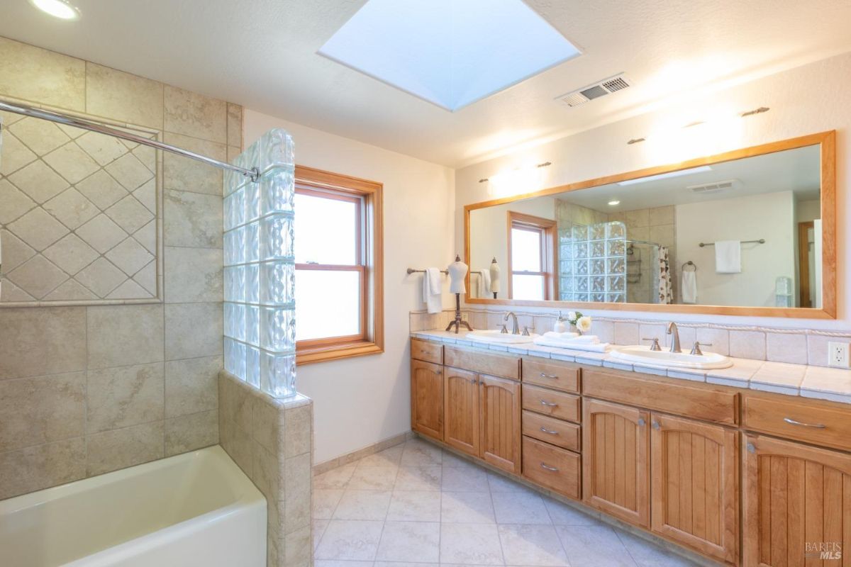 Bathroom with a glass-block divider, dual sinks, and tiled shower.