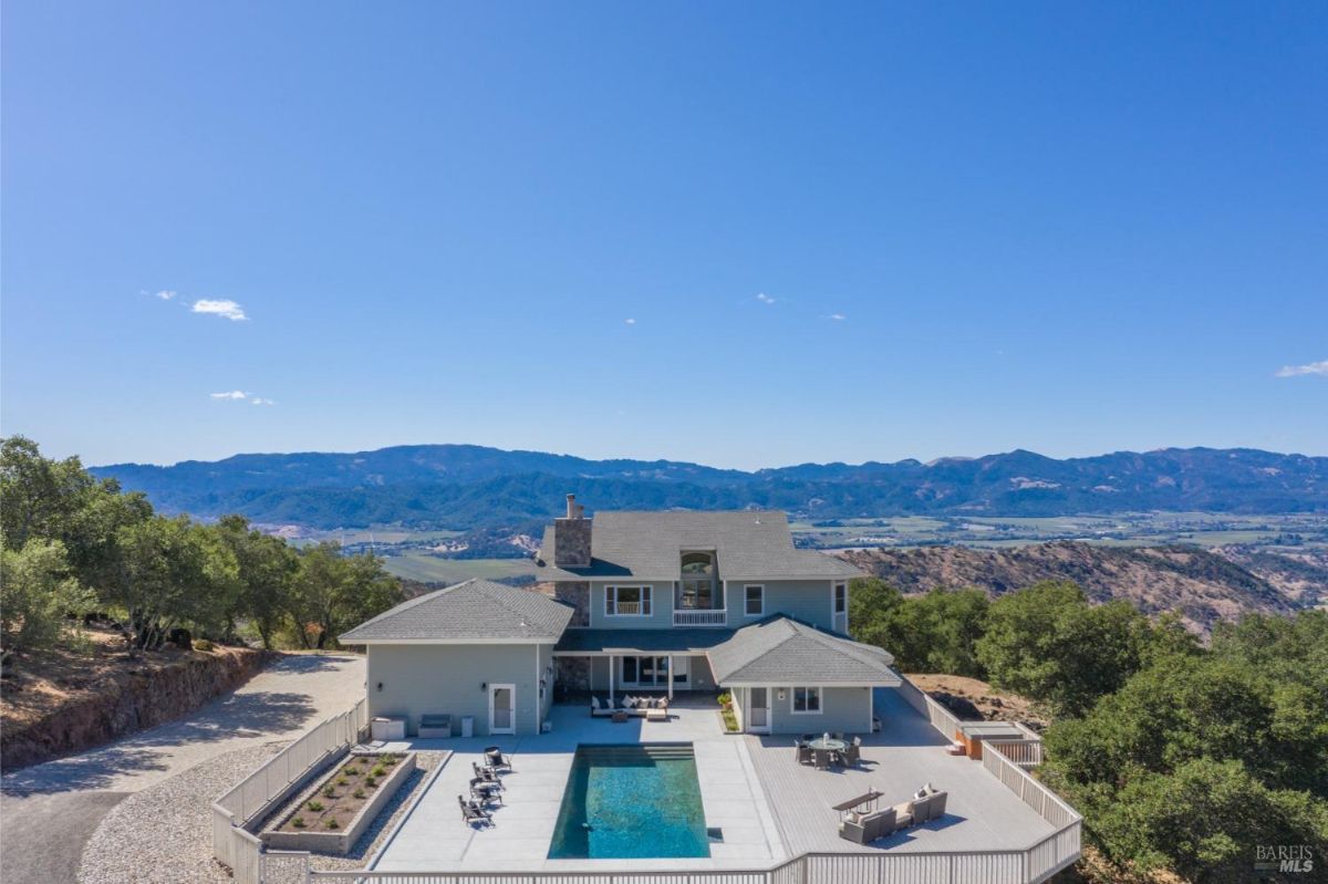 Exterior shot of a two-story house with a pool and deck overlooking a valley and mountains.