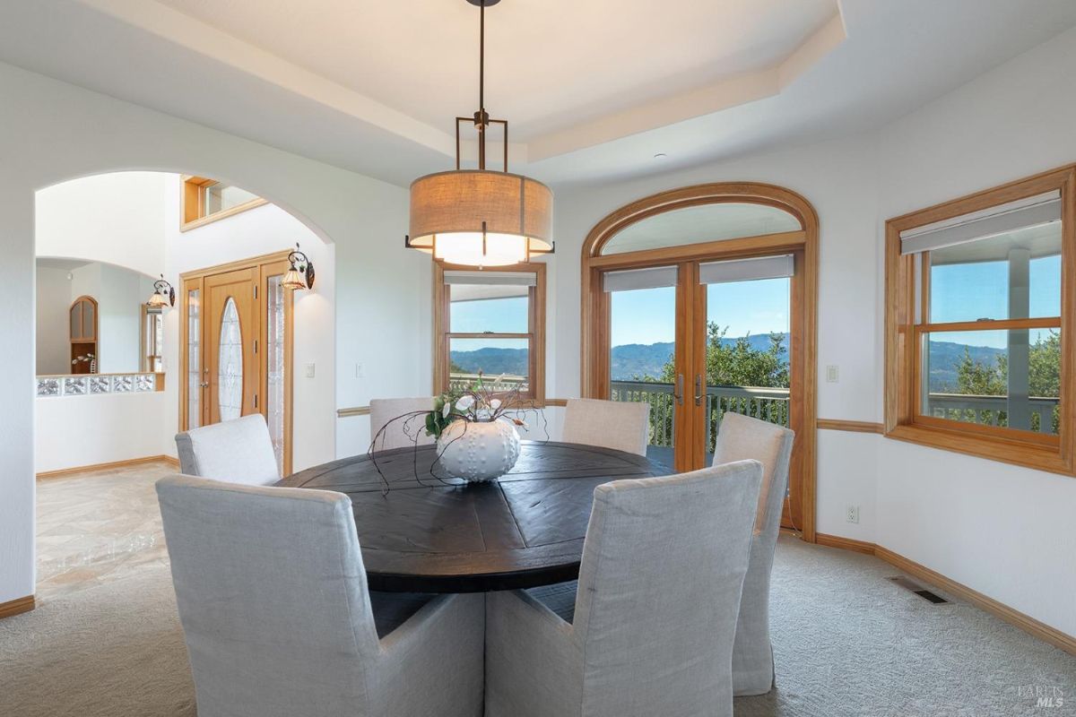 Round dining table with upholstered chairs situated near arched doorways and large windows.