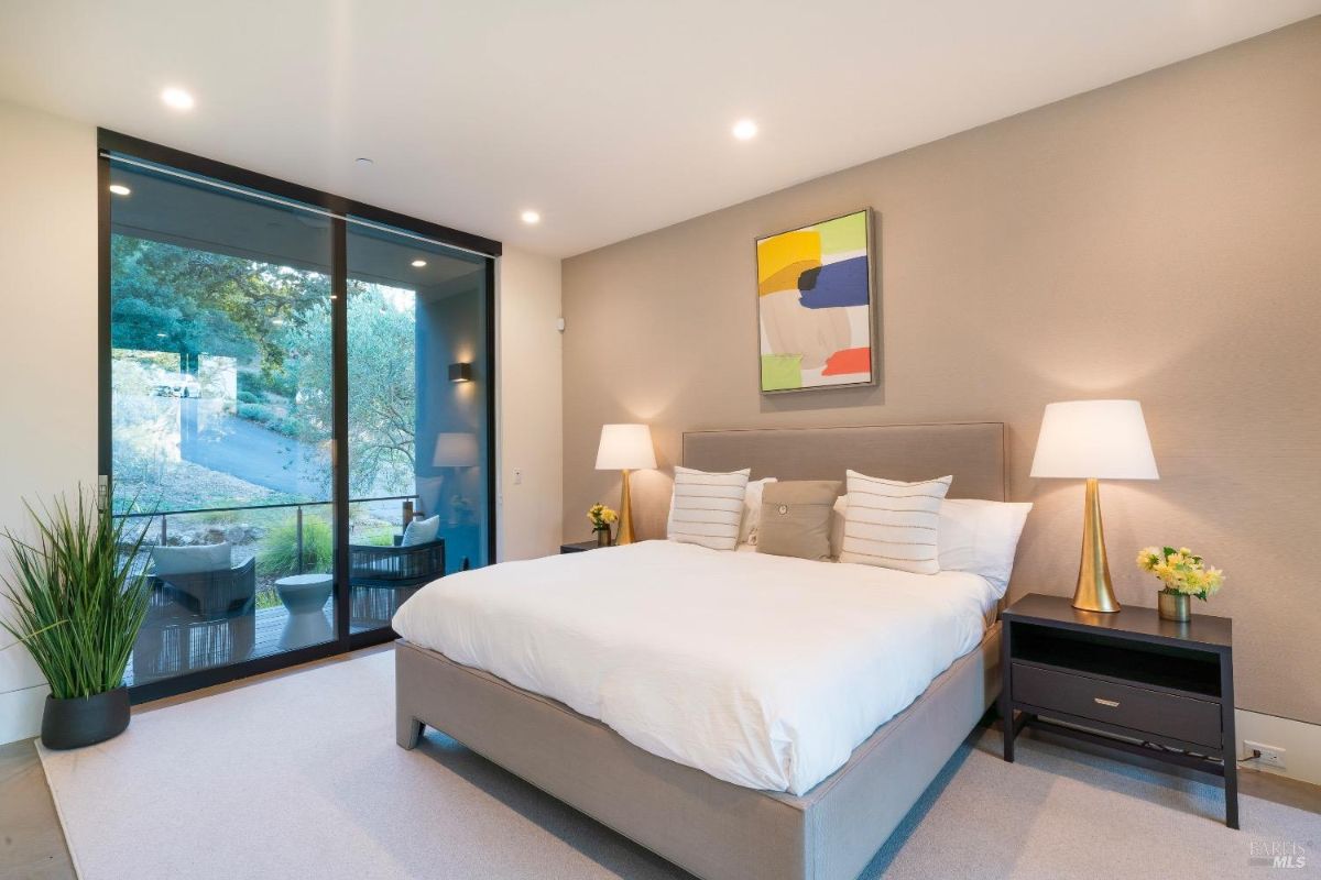 Bedroom features a large glass door leading to a private patio with outdoor seating. Neutral tones and modern art create a serene and contemporary atmosphere.