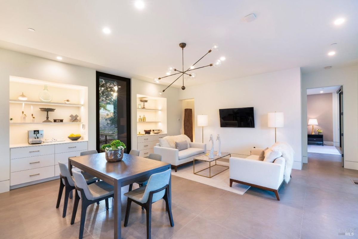 Open-concept living and dining area with built-in shelving and a sleek modern design. Neutral tones, recessed lighting, and a central chandelier create a balanced and inviting atmosphere.