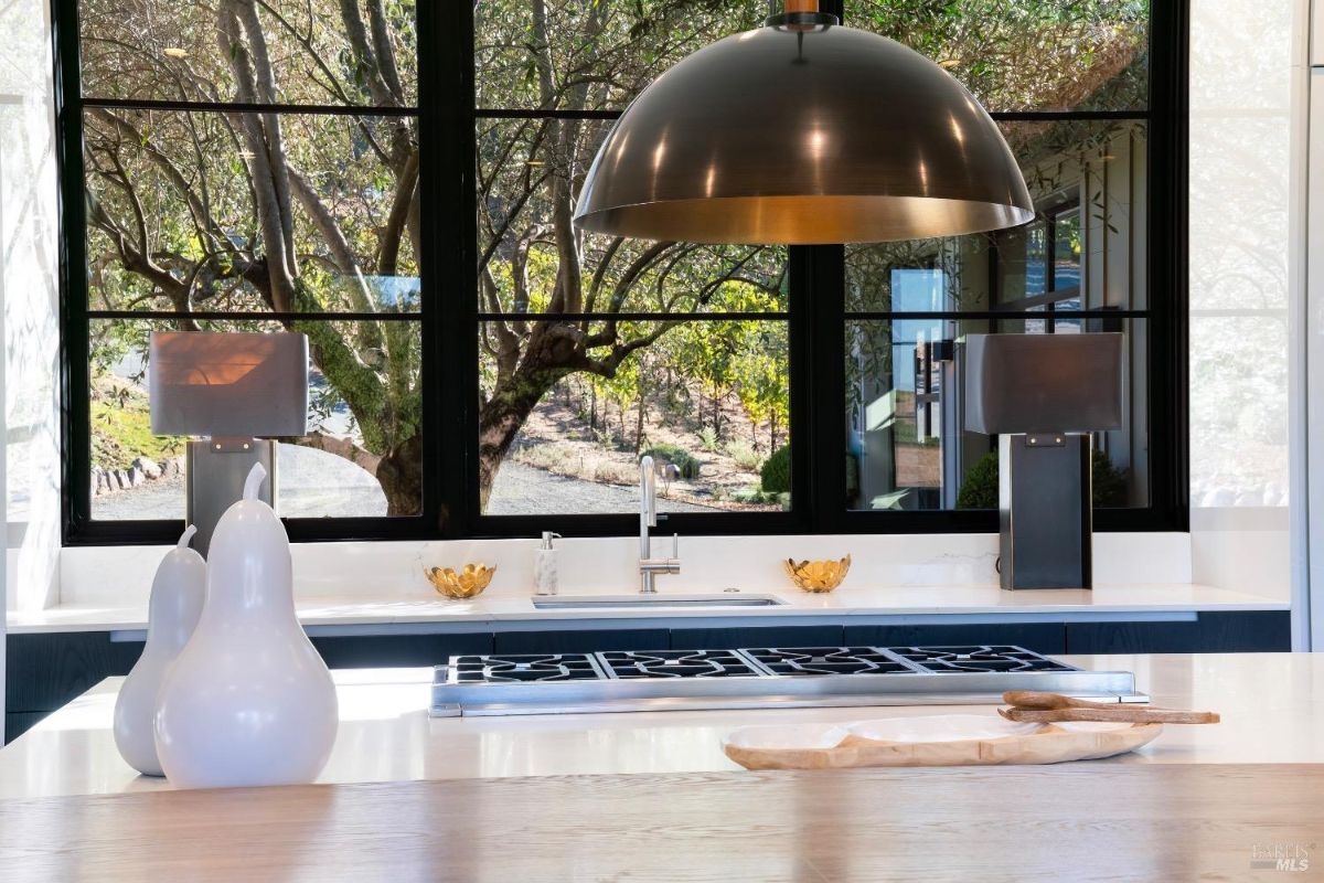 Kitchen features a large window providing natural light and views of outdoor greenery. Centerpiece includes a modern pendant light above a spacious island with a built-in gas cooktop.