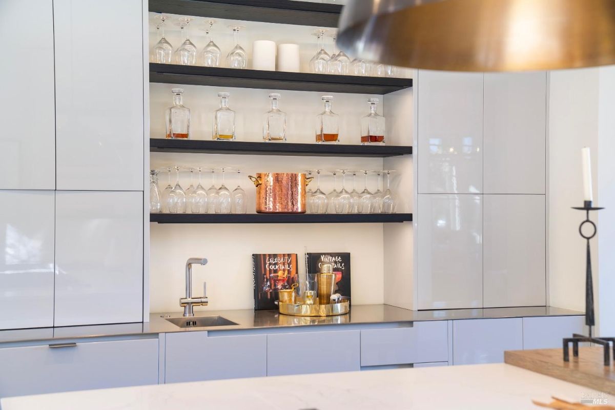 Bar area features open shelving with neatly arranged glassware and decanters. Compact sink and metallic accents provide functionality and elegance.