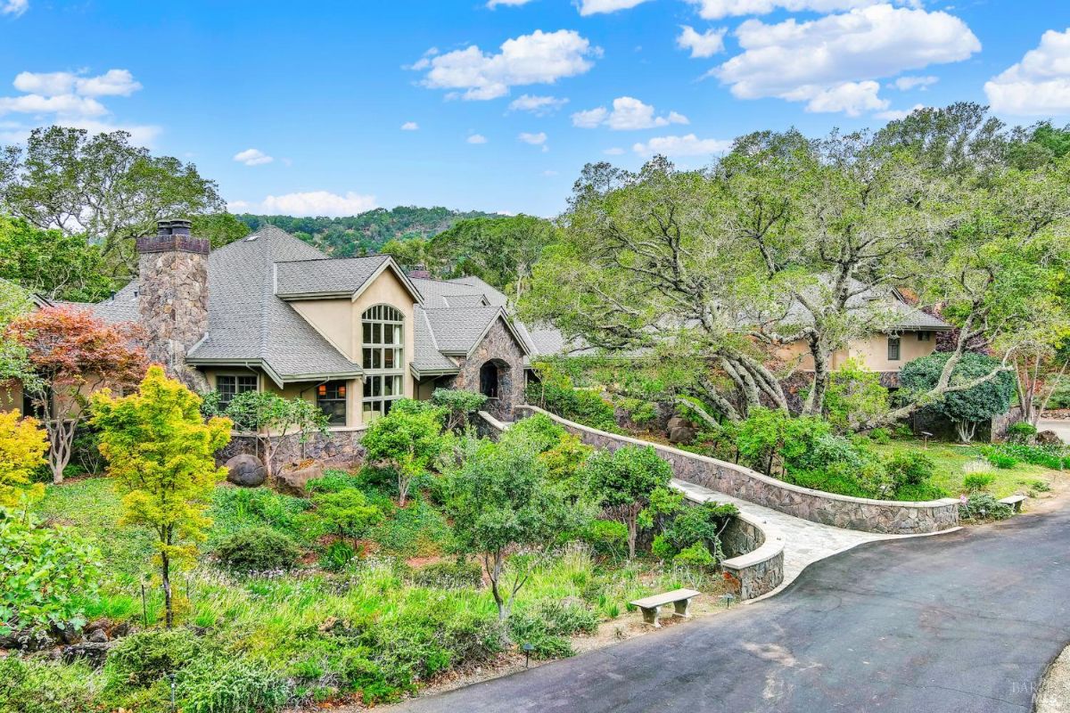 A stately home surrounded by lush greenery and stone pathways, featuring large windows and classic architecture.