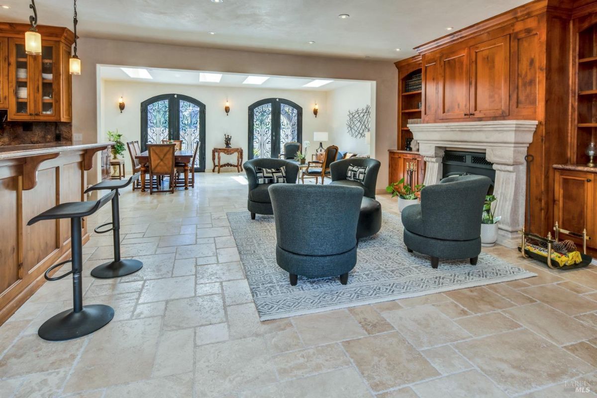 Open living space with bar stools at a counter, a seating area, and double doors leading to a dining space.