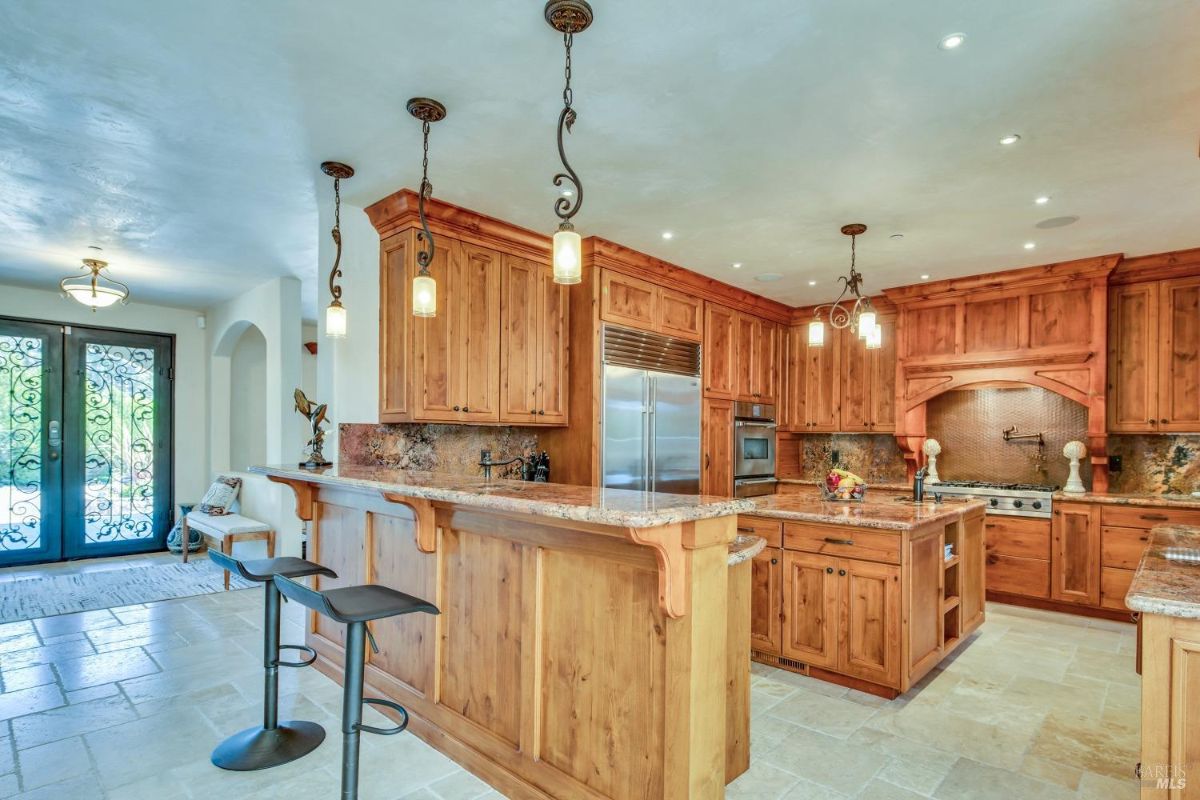 The kitchen features a large island, wooden cabinetry, and a breakfast bar with two stools.