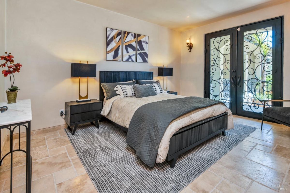 The bedroom features a bed with a black headboard, two nightstands, and a rug on the tile floor.