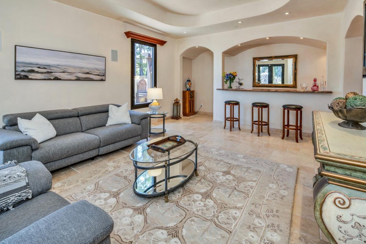 Lounge with a gray sectional sofa, a decorative bar counter, and glass-top tables on a patterned rug.