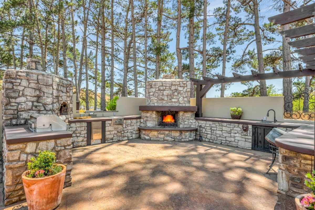 The outdoor kitchen features a stone pizza oven, a fireplace, and a grill.